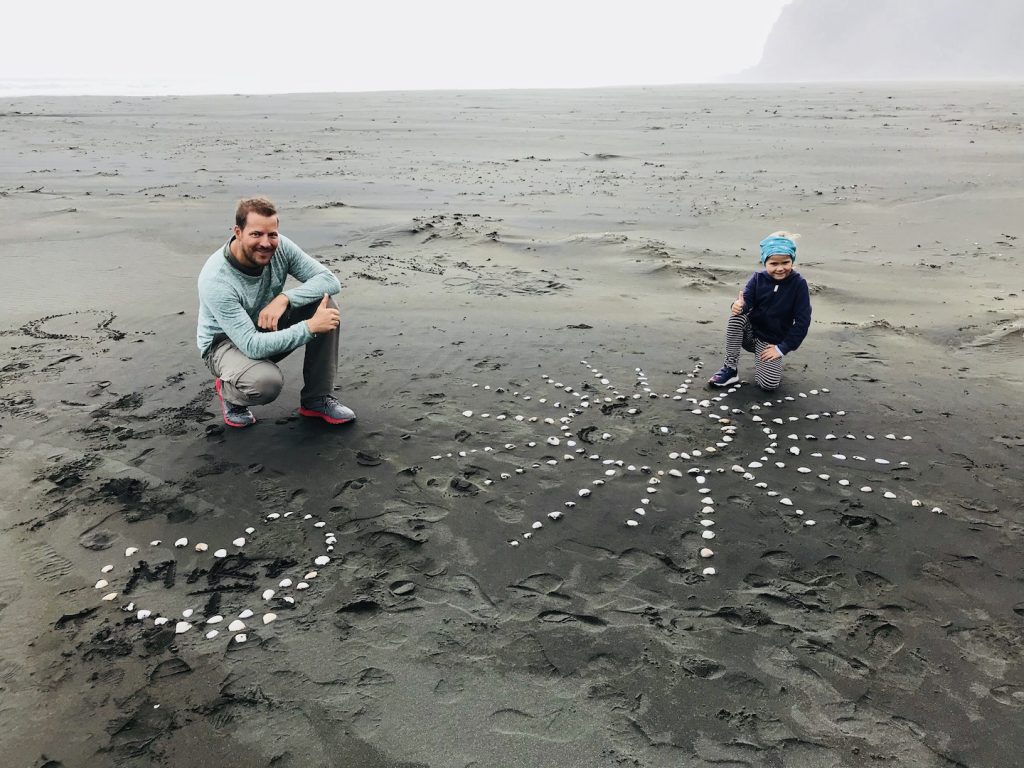 Vater und Tochter bauen Muschelbilder am Karekare Beach, Neuseeland