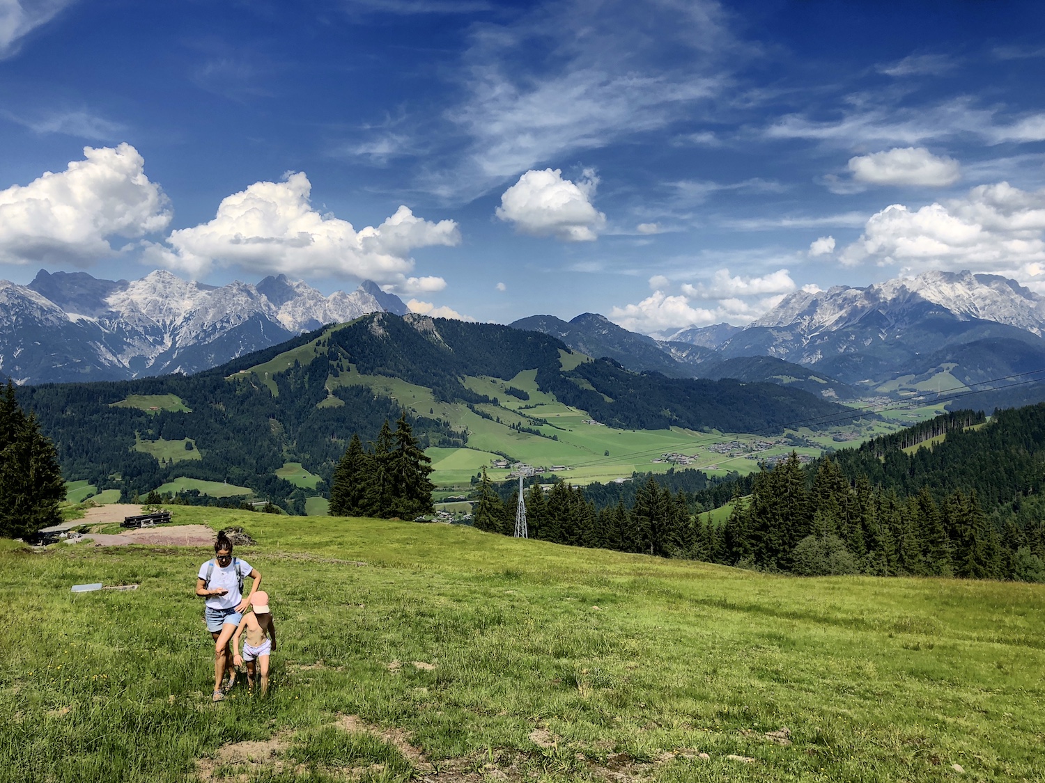 Frau und Kind wandern auf grüner Wiese, im Hintergrund die Berge, Tirol